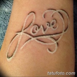 Фото белой татуировки надписи 'Love' с декоративными завитушками на запястье. Необычный стиль, привлекающий внимание.