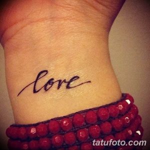 Фотография небольшой татуировки с надписью 'love' на запястье. Черный контур, простой и элегантный дизайн.