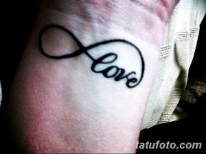 Фотография небольшой татуировки с надписью 'love' внутри символа бесконечности на запястье. Черный контур, простой дизайн.