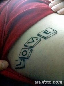 Фото тату на животе: надпись "Love" составленная из кубиков, как в игре Scrabble. Необычный и запоминающийся дизайн.