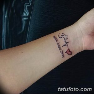 Фото тату на предплечье: надпись "faith, hope, love" с изображением символа Ом, кардиограммы и сердца. Лаконичный и символичный дизайн.