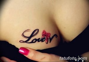 Фото тату надписи "Love" с красным бантиком, расположенной на груди. Элегантный шрифт и нежный дизайн делают татуировку женственной и романтичной.
