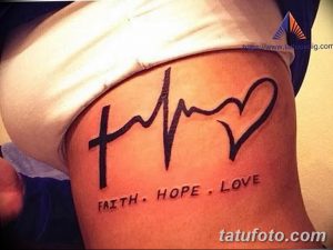 Фото тату: надпись 'Faith, Hope, Love' с изображением креста, сердца и волнистой линии на боку. Черный рисунок татуировки, символизирующий веру, надежду и любовь.