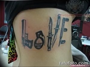 Фото тату: слово 'LOVE' на боку, буквы которого образованы из пистолета, ножа и гранаты. Черный рисунок татуировки, вызывающий и провокационный.