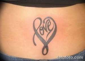 Фото тату на животе: надпись 'Love' стилизованная под форму сердца, выполненная черными чернилами.