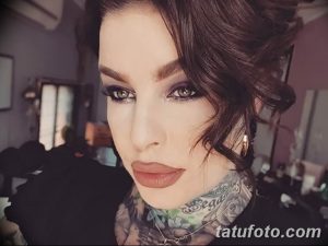 Фотография девушки с темными волосами, украшенной татуировками на шее и груди, с ярким макияжем и выразительными глазами.