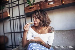 Фотография девушки, наслаждающейся пиццей, с видимыми татуировками на плече и запястье. Девушка выглядит счастливой и беззаботной.