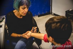 Фото процесса создания татуировки: мастер тату делает татуировку ребенку на руке, используя тату-машинку.