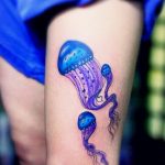 Фото акварельной татуировки двух медуз на бедре. Яркие синие и фиолетовые цвета, плавные переходы, детализированные щупальца.