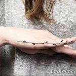 Фото тату: тонкая черная веточка с листьями, обвивающая тыльную сторону руки. Минималистичный рисунок татуировки выполнен в технике лайнарт.