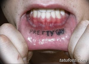 Фото тату: надпись 'PRETTY GAY' черными чернилами на внутренней стороне губы. Необычное и провокационное решение для самовыражения.