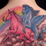 Фото тату двух мифических существ: единорога и пегаса, на спине человека. Радужный фон, яркие цвета, сказочный рисунок татуировки.