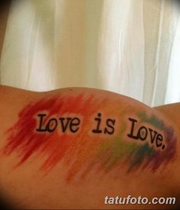 Фото тату с надписью 'Love is Love', выполненной черным цветом на фоне красочных акварельных разводов красного, зеленого и синего.