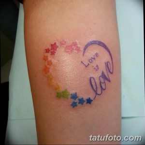 Фото тату на предплечье: надпись 'Love is Love' в радужном сердце, украшенном звездами. Романтичный и символичный рисунок татуировки.