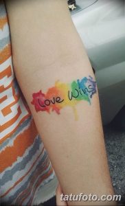 Фото тату на предплечье с надписью 'Love Wins' и разноцветными акварельными брызгами.