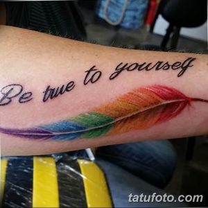 Фото тату: татуировка в виде пера, окрашенного в цвета радуги, с надписью 'Be true to yourself' на руке.