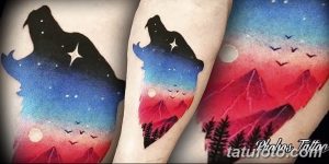 Фото тату: красивая акварельная татуировка с изображением волка, силуэт которого выполнен на фоне ночного неба с горами и звездами.