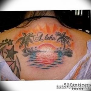 Фото тату на лопатке с изображением тропического заката, пальм и надписи 'Aloha'. Яркие оранжевые и красные оттенки неба.