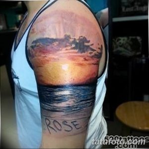 Фото татуировки с изображением морского заката, волн и надписи 'ROSE' на плече.