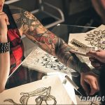 Фотография процесса создания татуировки: мастер рисует эскиз на руке клиента, рука клиента украшена уже готовыми татуировками.