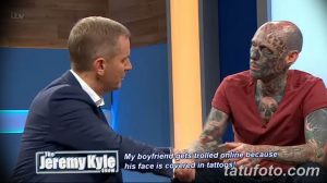 Мужчина с полностью татуированным лицом сидит в студии и разговаривает с ведущим. Фотография сделана во время телешоу.