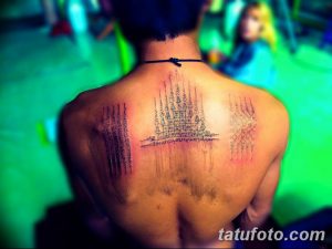 Фото татуировки на спине, состоящей из множества традиционных тайских символов и изображений Будды. Черно-белый рисунок.
