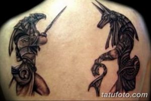 Фото татуировки с двумя фигурами Анубиса, одна в атакующей позе, другая в защитной. Рисунок выполнен в черно-серых тонах с детализированной прорисовкой.