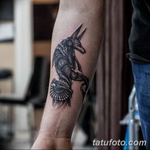 Черно-серая татуировка Анубиса на предплечье. Детализированное изображение египетского бога с головой шакала, выполненное в реалистичном стиле.