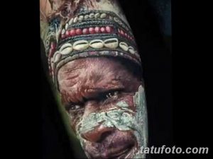 Фото тату на руке: реалистичное изображение лица пожилого индейца с морщинами и традиционной раскраской, выполненное в черно-серых тонах с высокой детализацией.