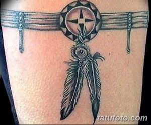 Фото тату: татуировка в стиле Native American, изображающая ловчий круг с пером, выполненная в черно-серых тонах на руке.