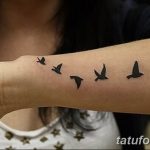 Фото тату на запястье: минималистичное изображение стаи из пяти черных птиц в полете, выполненное тонкими линиями.