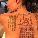 Фотография спины женщины, покрытой сложными тайскими татуировками, включающими священные символы и текст.