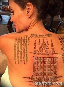 Фотография спины женщины, покрытой сложными тайскими татуировками, включающими священные символы и текст.