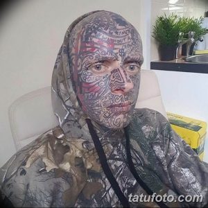 Фото татуировки, демонстрирующее полное покрытие лица и тела мужчины сложными черными узорами. Рисунок выполнен в стиле, сочетающем элементы трайбл и графики.