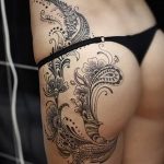 Фото тату мехенди на женском бедре, выполненное в черном цвете. Рисунок состоит из сложных растительных узоров и геометрических фигур.