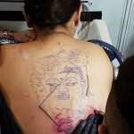 Фото тату: эскиз татуировки Будды на спине женщины, выполненный в нежных пастельных тонах.