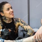 Фото тату: молодая женщина-мастер тату делает татуировку клиенту, ее руки покрыты яркими рисунками.