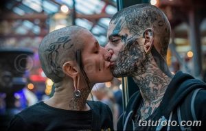 Фото пары с татуировками: лица и тела полностью покрыты сложными черными узорами. Пара целуется, демонстрируя свой экстремальный боди-арт.
