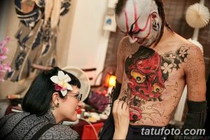 Фото тату: мастер наносит татуировку в японском стиле на спину клиента. Крупный план процесса нанесения рисунка.