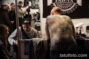 Фото процесса нанесения татуировки на спине клиента, мастер работает над сложным рисунком с черепом.