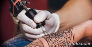 Фото процесса нанесения татуировки, мастер работает над татуировкой на руке клиента, используя тату-машинку.