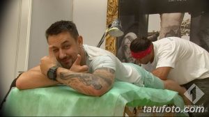 Фото процесса нанесения татуировки, мастер работает над татуировкой на теле клиента, клиент лежит на кушетке.