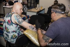 Фотография мастера тату, работающего над татуировкой на руке клиента. Видны инструменты, чернила и процесс нанесения рисунка.
