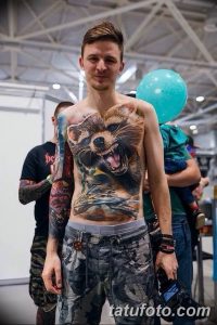 Фотография мужчины с масштабной татуировкой медведя на груди и теле. Реалистичный рисунок, детализированная прорисовка шерсти и глаз.