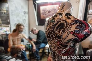 Фотография татуировки в японском стиле на манекене. Изображение карпа кои, волн и цветов. Детализированный рисунок и яркие цвета.
