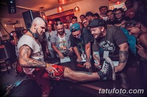 Фотография с тату-конвента, где мастер тату демонстрирует свою работу группе заинтересованных людей.