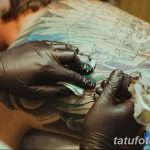 Фотография процесса нанесения масштабной татуировки на спину клиента, мастер в перчатках работает над деталями рисунка.