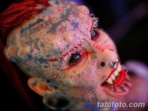 Фотография девушки с экстремальными татуировками на лице, включая пирсинг и рисунки, демонстрирующая смелый и провокационный боди-арт.