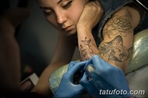 Фото тату: процесс нанесения татуировки на руку девушки. Виден мастер с тату-машинкой и рука девушки с эскизом.