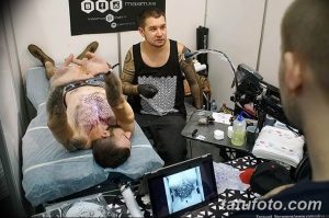 Фото тату: мастер тату делает татуировку мужчине на груди, на экране планшета виден эскиз.